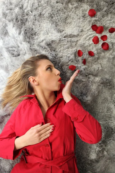 Женщина в красном лежит на ковре и дует лепестки роз — стоковое фото
