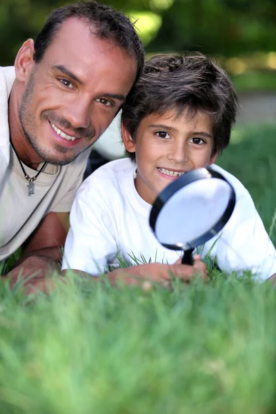 Vader en zoon onderzoeken het gras met een vergrootglas — Stockfoto