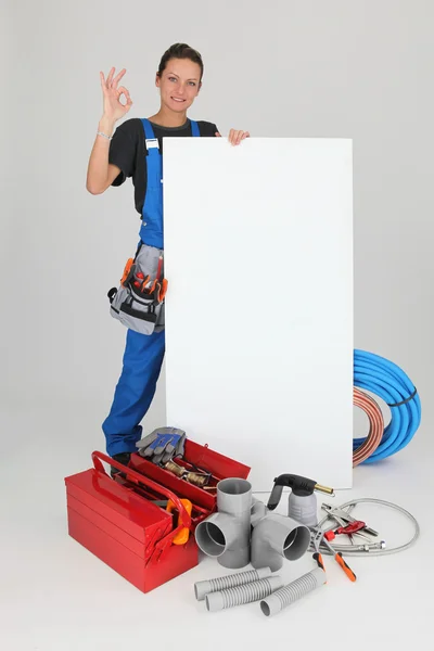 Encanador feminino com ferramentas do comércio e uma placa deixou em branco para sua mensagem — Fotografia de Stock