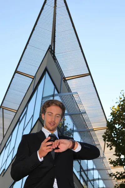 Giovane uomo d'affari che controlla il telefono e guarda fuori da un edificio moderno — Foto Stock