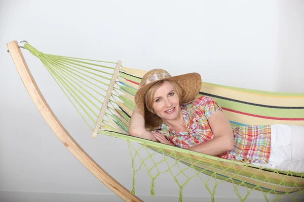 Studio shot of a woman in a straw hat lounging on a striped hammock — Stock Photo, Image