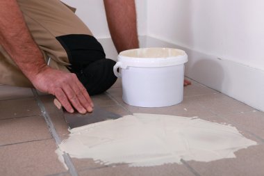 Man applying adhesive over an old tiled floor clipart