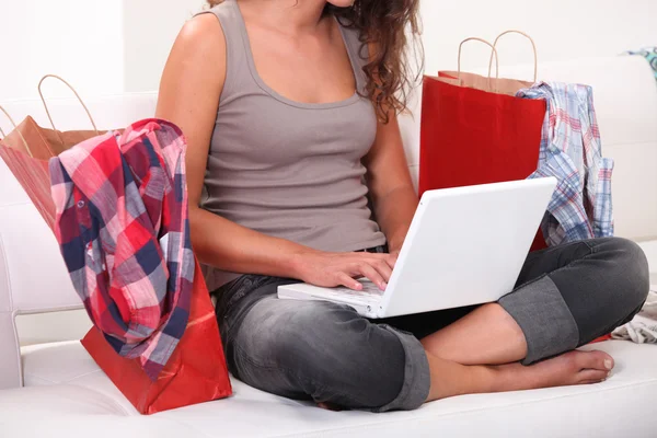 Mulher sentada no sofá com computador e sacos — Fotografia de Stock