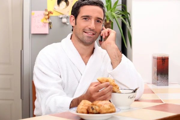 Giovane uomo che fa una chiamata mentre fa colazione — Foto Stock