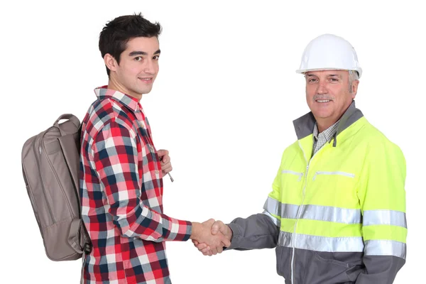 Young apprentice with backpack shaking hands with senior foreman — Stock Photo, Image