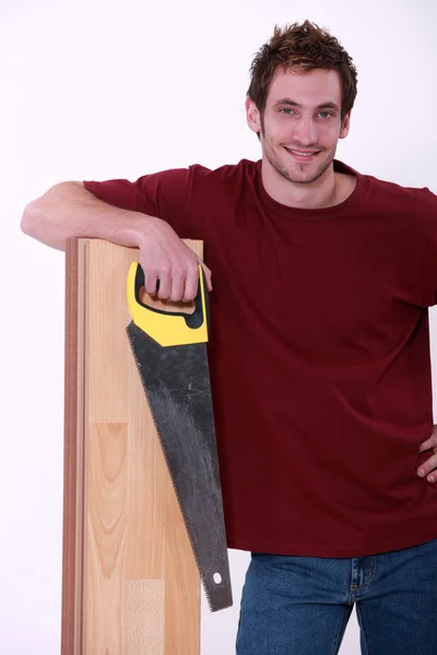 Testere holding ve ahşap bir floorboard üzerinde yaslanmış bir adam — Stok fotoğraf