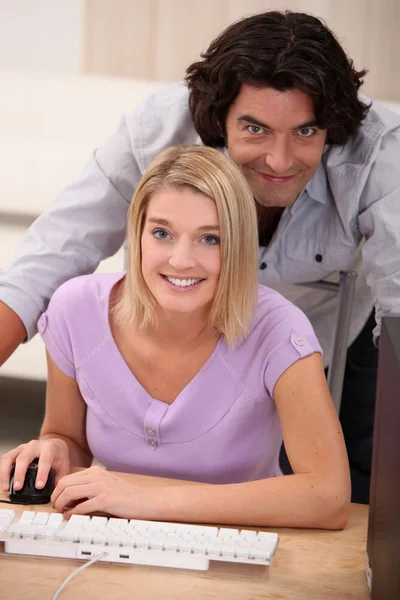 Una mujer rubia haciendo el ordenador y su marido frente a la cámara — Foto de Stock