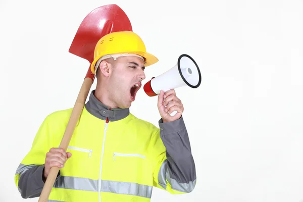 Worker with a spade screaming into a bullhorn — Stock Photo, Image
