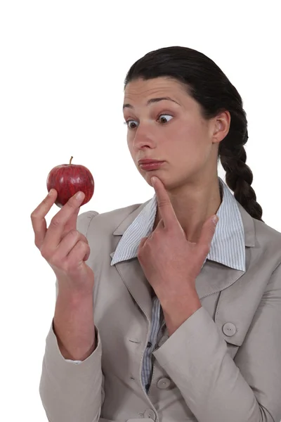 Eine Geschäftsfrau blickt seltsam auf einen Apfel. — Stockfoto