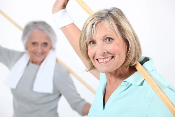 Oudere vrouwen die zich uitstrekt met houten paal — Stockfoto