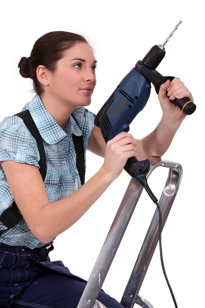 Woman holding drill whilst climbing ladder — Stock Photo, Image