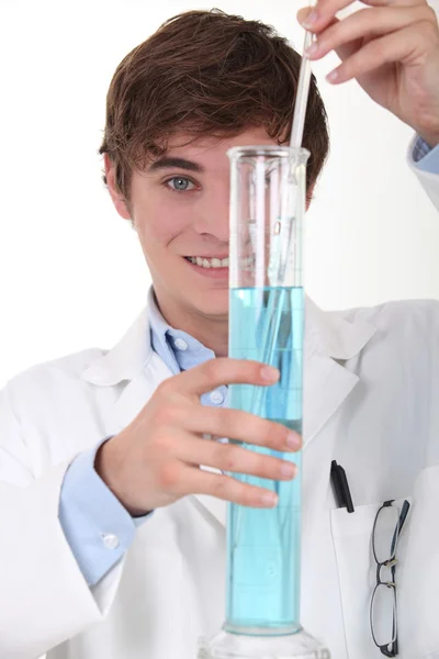 Young chemistry student stirring blue liquid in a glass graduated cylinder — Stock Photo, Image