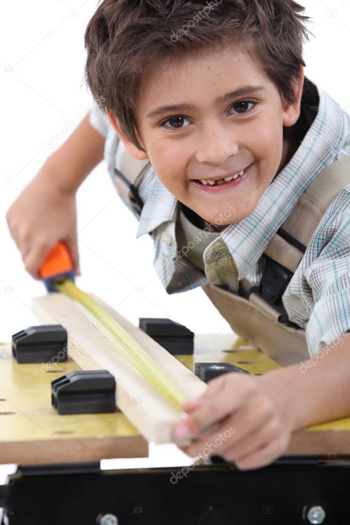 Niño midiendo un trozo de madera para cortar 2023