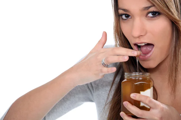 Brunette dipping finger in honey jar — Stock Photo, Image