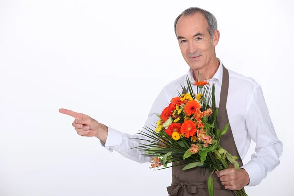 65 jaar oude mannelijke bloemist nemen een boeket bloemen en vinger wijzen op iets — Stockfoto