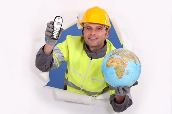 Happy-looking builder holding globe and cordless phone — Stock Photo, Image