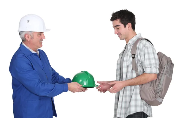 Construtor entregando chapéu duro para o jovem trabalhador — Fotografia de Stock
