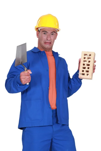 Mason holding a trowel and a brick and looking disgusted — Stock Photo, Image