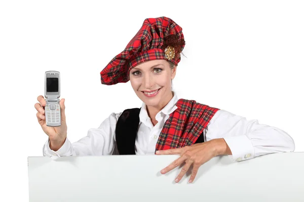 Woman in a Scottish outfit with a mobile phone and a board left blank for your message — Stock Photo, Image