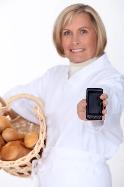 Baker segurando seu telefone celular e uma cesta de baguetes — Fotografia de Stock