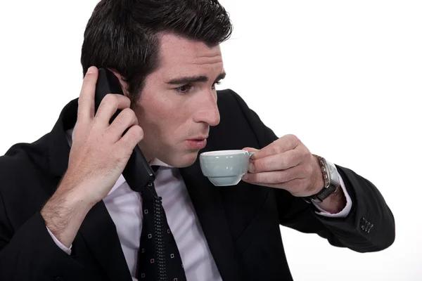 Podnikatel, rychle se snaží mluvit o telefonu při pití šálek kávy — Stock fotografie