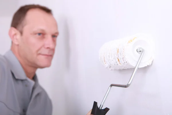 Decorador pintando uma sala branca com o rolo em primeiro plano — Fotografia de Stock
