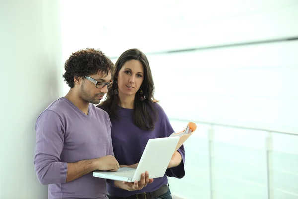 Collega's op zoek naar een laptop en papier-bestanden in een gang — Stockfoto