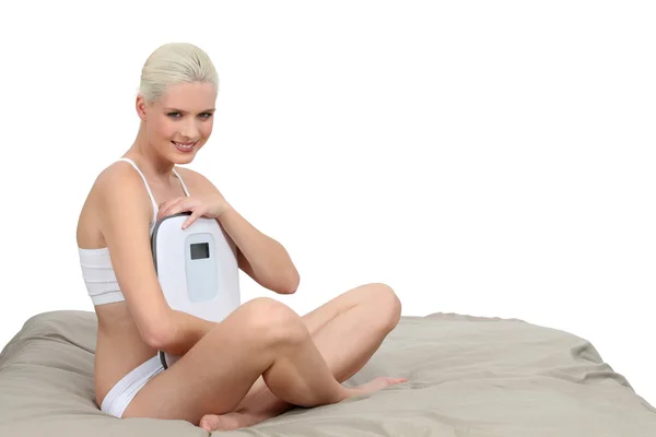 Blonde woman on bed with a weighing machine — Stock Photo, Image