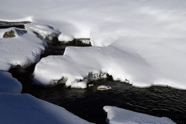 Um fluxo de água cortando através de snowdrifts — Fotografia de Stock