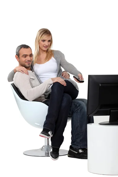 Woman sitting on the knees of her boyfriend and watching television — Stock Photo, Image