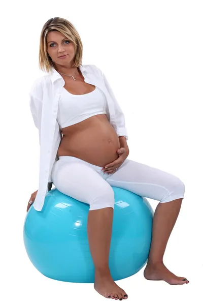 Kobieta w ciąży trzymając jej brzuch i siedzi na ćwiczenia piłka — Zdjęcie stockowe