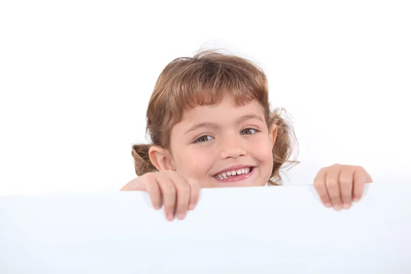 Little blonde girl laughing is half hidden behind a white panel — Stock Photo, Image