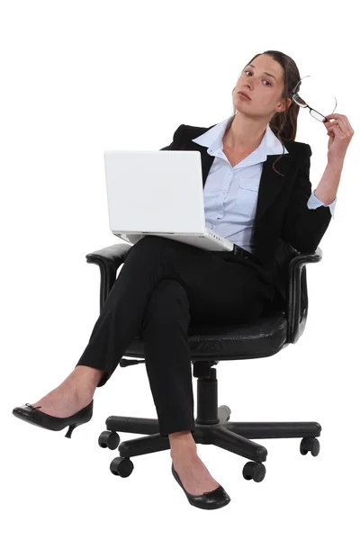 Confident businesswoman sitting cross-legged on chair with laptop Stock Image