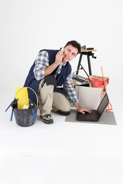 Tiler kneeling by equipment while on the phone — стоковое фото