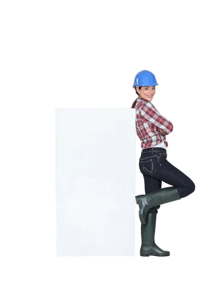 Tradeswoman leaning against a blank sign — 스톡 사진