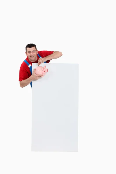 Craftsman holding a pig bank and a blank poster — Stock Photo, Image