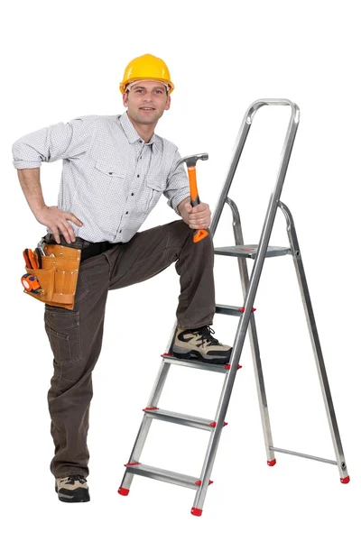 Плотник с ногой, опирающийся на лестницу, держа молоток — стоковое фото