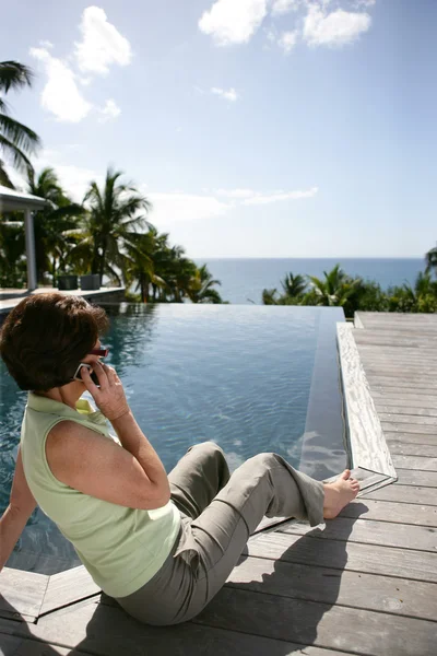 Ανώτερος γυναίκα που πραγματοποιείτε μια κλήση δίπλα στην πισίνα — Φωτογραφία Αρχείου