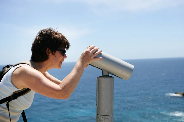 Mujer mirando a través de telescopio público en la costa — Stockfoto