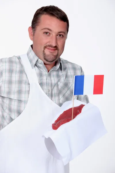 Açougueiro segurando um pedaço de bife cravado com a bandeira francesa — Fotografia de Stock