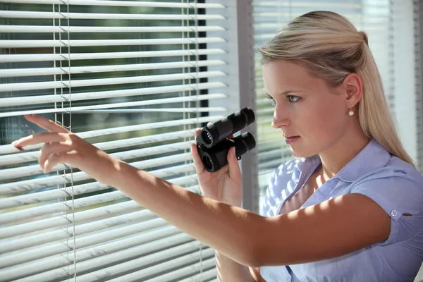 Frau blickt mit Fernglas durch die Jalousien — Stockfoto