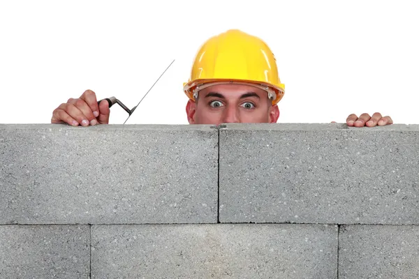 Bricklayer peering over a wall — Stockfoto