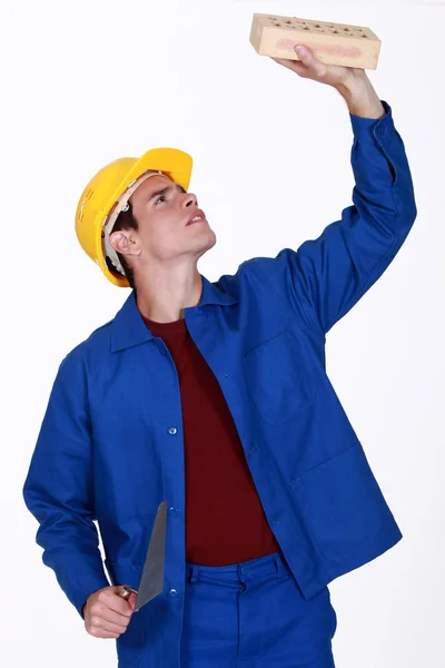Young bricklayer in jumpsuit inspecting brick — Stock Photo, Image