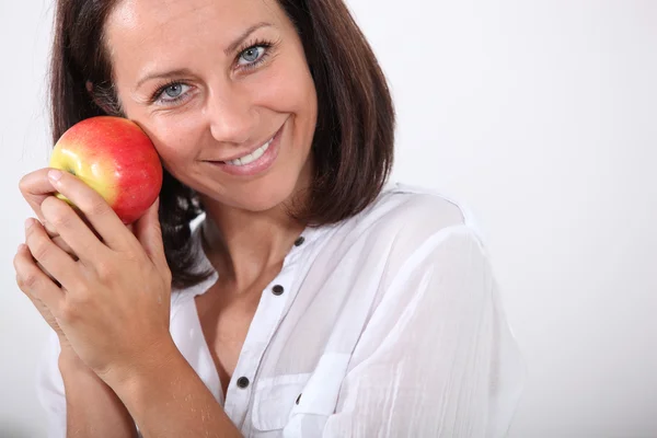 Mujer sonriente sosteniendo una manzana en su cara — Foto de Stock