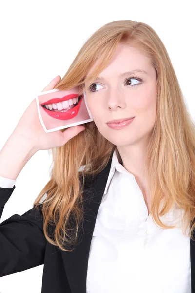 Mujer joven sosteniendo una foto de una boca al lado de su oreja —  Fotos de Stock