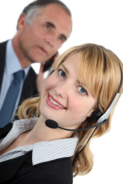 Giovane receptionist con auricolare e boss in background — Foto Stock