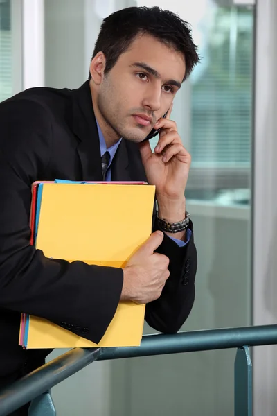 Serious businessman talking on his mobile phone and holding files — Stock Photo, Image
