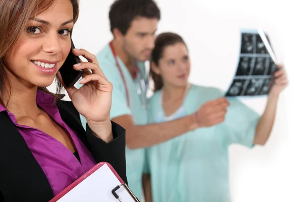 Ziekenhuis manager op een telefoon als dokters kijken naar x-stralen in de achtergrond — Stockfoto