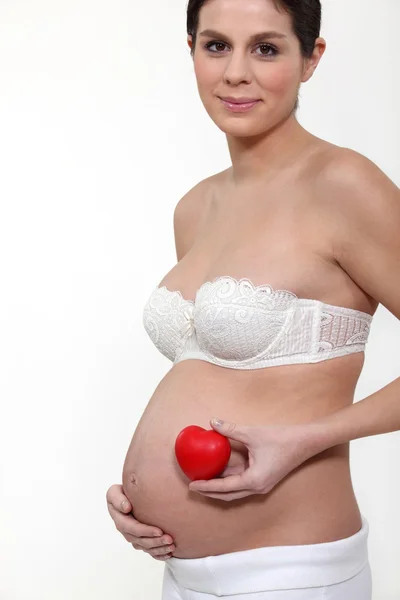Mulher grávida em roupa interior segurando caixa em forma de coração — Fotografia de Stock