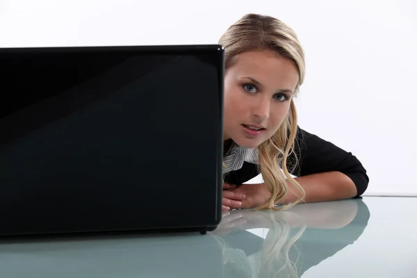 Mujer espiando alrededor de un ordenador portátil — Foto de Stock
